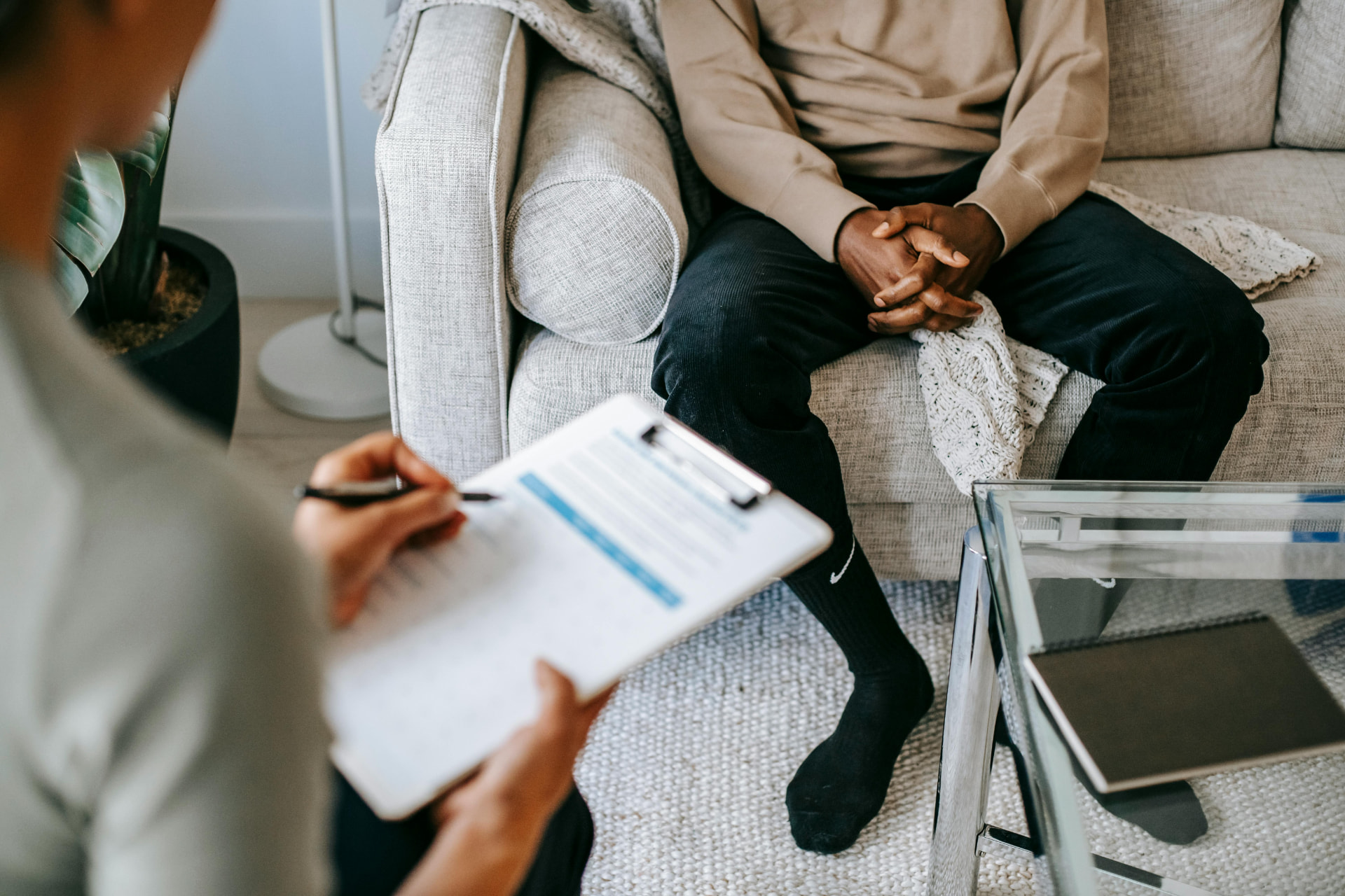 A client seated on a couch in session while a therapist takes notes